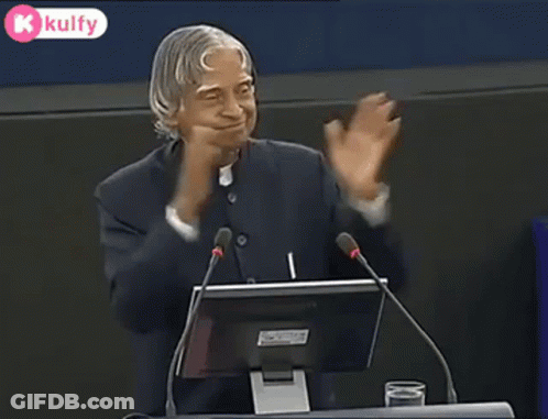 A Man Is Giving A Speech In Front Of A Microphone And A Computer Monitor . GIF