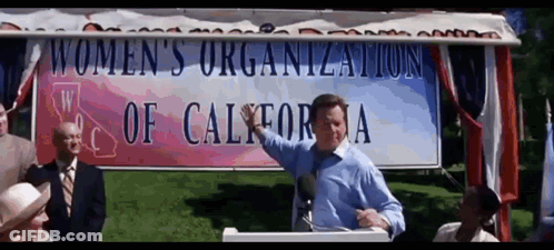 A Man Is Giving A Speech In Front Of A Women 'S Organization Of California Sign GIF