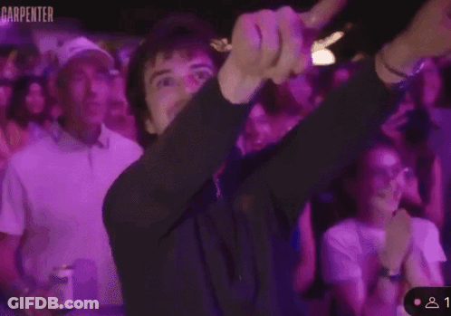 A Man Is Giving A Thumbs Up In Front Of A Crowd With The Word Carpenter On The Bottom Right GIF