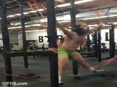 A Man Is Hanging From A Bar In A Gym While Wearing Green Underwear . GIF