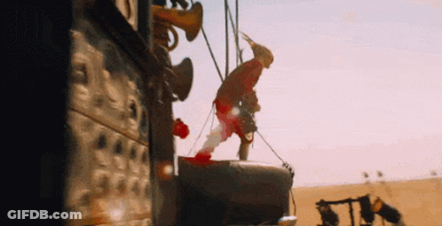 A Man Is Hanging From A Rope In The Desert While Wearing A Hat . GIF