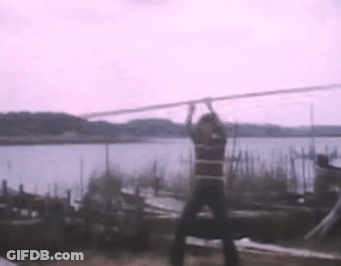 A Man Is Hanging From A Rope Overlooking A Body Of Water . GIF
