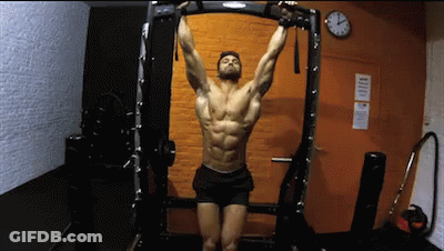 A Man Is Hanging Upside Down On A Bar In A Gym . GIF