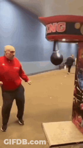 A Man Is Hitting A Punching Bag In A Boxing Machine GIF