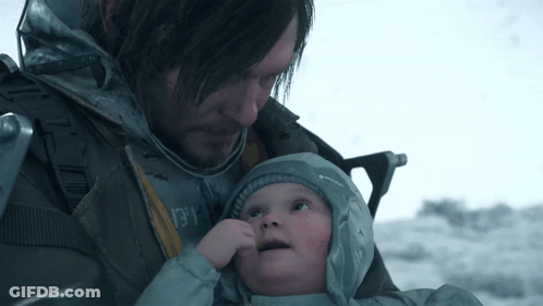 A Man Is Holding A Baby In His Arms And The Baby Is Wearing A Grey Jacket With The Word Columbia On It GIF