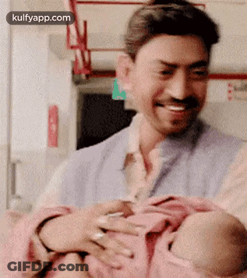 A Man Is Holding A Baby In His Arms While Smiling . GIF