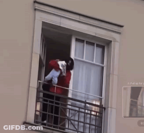 A Man Is Holding A Baby In His Arms While Standing On A Balcony GIF