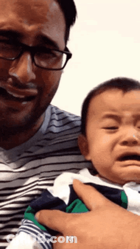 A Man Is Holding A Baby Who Is Crying And The Letter M Is Above Him GIF