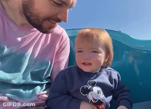 A Man Is Holding A Baby Who Is Wearing A Mickey Mouse Sweatshirt GIF