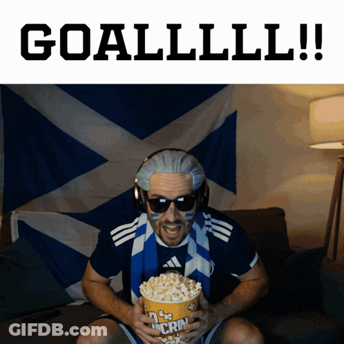 A Man Is Holding A Bag Of Popcorn With The Words Goallll !! Behind Him GIF