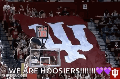 A Man Is Holding A Basketball Hoop In Front Of A Large Banner That Says We Are Hoosier ! GIF