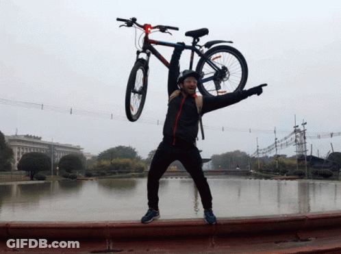 A Man Is Holding A Bicycle Over His Head And Pointing At The Camera GIF