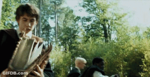 A Man Is Holding A Book In Front Of A Group Of People . GIF