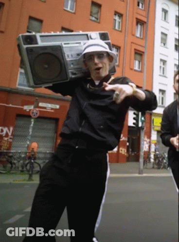 A Man Is Holding A Boombox Over His Head In Front Of A Building That Says Dn GIF