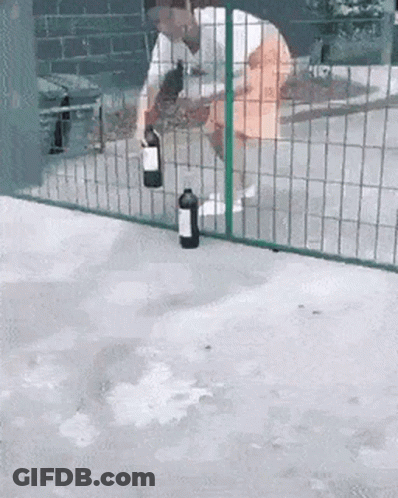 A Man Is Holding A Bottle Of Wine In Front Of A Fence GIF