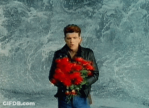 A Man Is Holding A Bouquet Of Red Flowers In His Hands . GIF