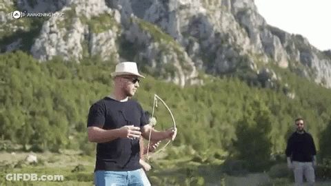 A Man Is Holding A Bow And Arrow In A Field . GIF