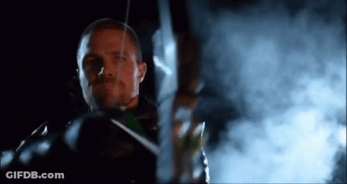 A Man Is Holding A Bow And Arrow In Front Of A Smokey Background . GIF
