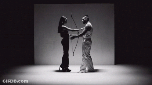 A Man Is Holding A Bow And Arrow While A Woman Holds A Bow And Arrow GIF