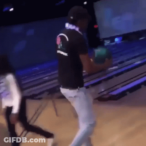 A Man Is Holding A Bowling Ball In A Bowling Alley While Wearing Headphones GIF