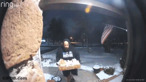 A Man Is Holding A Box Of Pizza In Front Of A Ring Doorbell . GIF