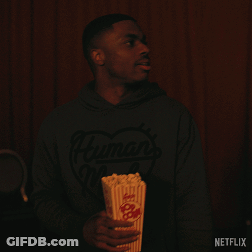A Man Is Holding A Bucket Of Popcorn With A Netflix Logo In The Corner GIF