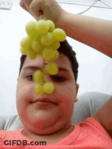 A Man Is Holding A Bunch Of Grapes Over His Face . GIF