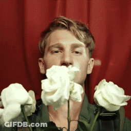A Man Is Holding A Bunch Of White Roses In Front Of His Mouth GIF
