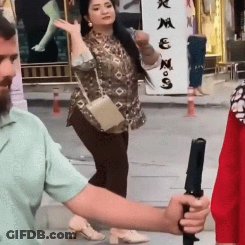 A Man Is Holding A Camera While A Woman Stands In Front Of A Sign That Says ' N ' On It GIF