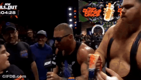 A Man Is Holding A Can Of Red Bull In Front Of A Crowd At A Wrestling Event . GIF