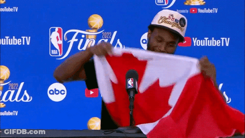 A Man Is Holding A Canadian Flag In Front Of A Microphone GIF