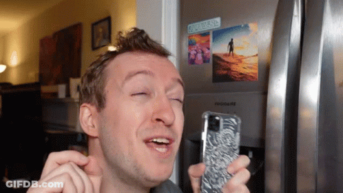 A Man Is Holding A Cell Phone In Front Of A Frigidaire Refrigerator GIF