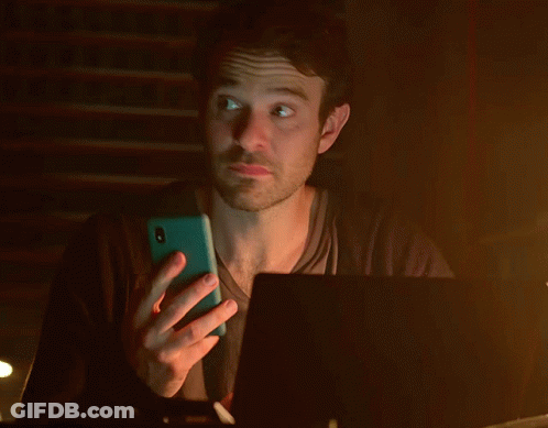 A Man Is Holding A Cell Phone In Front Of A Laptop Computer GIF