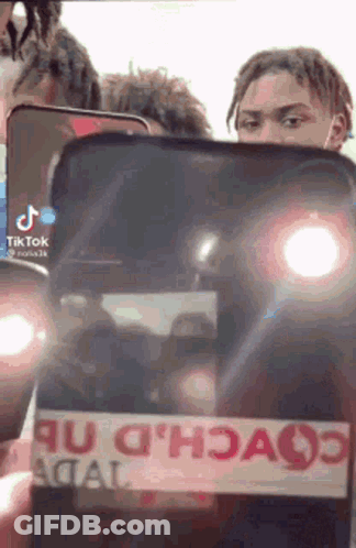 A Man Is Holding A Cell Phone With A Tik Tok Logo On It . GIF