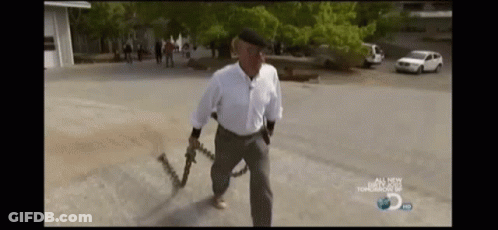 A Man Is Holding A Chain Around His Waist While Walking Down A Street . GIF