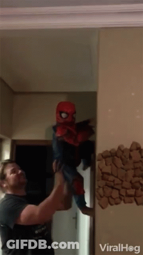 A Man Is Holding A Child In A Spiderman Costume In Front Of A Wall That Says Viralhog GIF