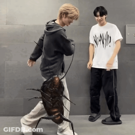 A Man Is Holding A Cockroach While Another Man Stands Next To Him . GIF