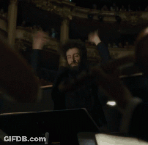A Man Is Holding A Conductor 'S Baton In His Hands In A Dark Room GIF