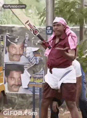 A Man Is Holding A Cricket Bat In Front Of A Wall With Posters Of Actors On It . GIF