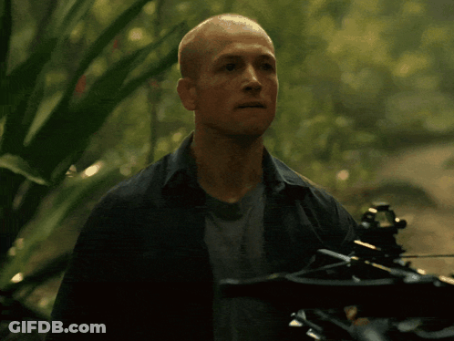 A Man Is Holding A Crossbow In The Woods And His Mouth Is Open GIF
