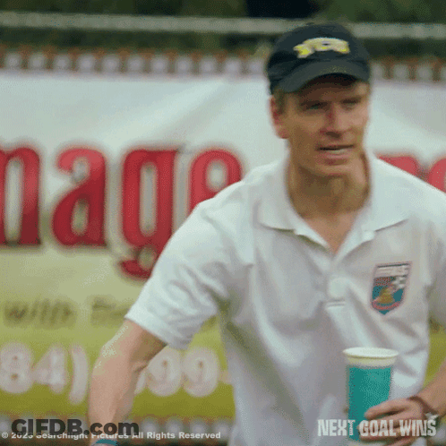 A Man Is Holding A Cup In Front Of A Sign That Says " Next Goal Wins " GIF
