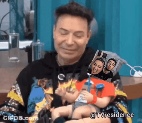 A Man Is Holding A Doll With A Picture Of A Man And A Woman Behind Him GIF