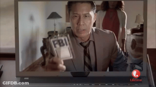 A Man Is Holding A Fbi Badge In Front Of A Laptop GIF