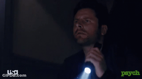 A Man Is Holding A Flashlight In A Dark Room With A USA Logo In The Corner GIF