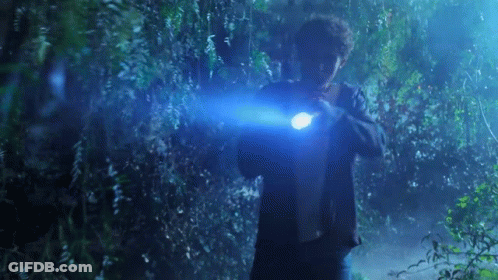 A Man Is Holding A Flashlight In His Hand In A Dark Forest . GIF