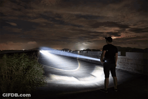 A Man Is Holding A Flashlight While Standing On A Bridge GIF