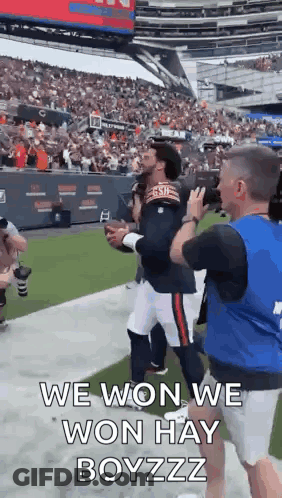 A Man Is Holding A Football In A Stadium And A Man Is Taking A Picture Of Him . GIF