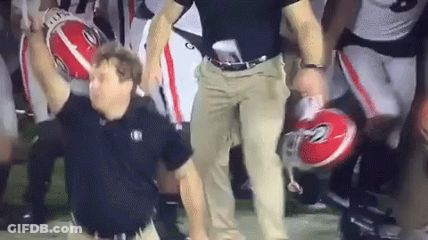 A Man Is Holding A Football In His Hand While A Group Of Football Players Are Standing Behind Him Holding Helmets . GIF