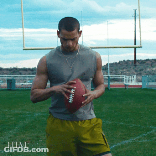A Man Is Holding A Football On A Field And The Word Him Is On The Bottom GIF
