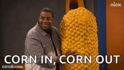 A Man Is Holding A Giant Corn On The Cob With The Words Corn In Corn Out Below Him GIF